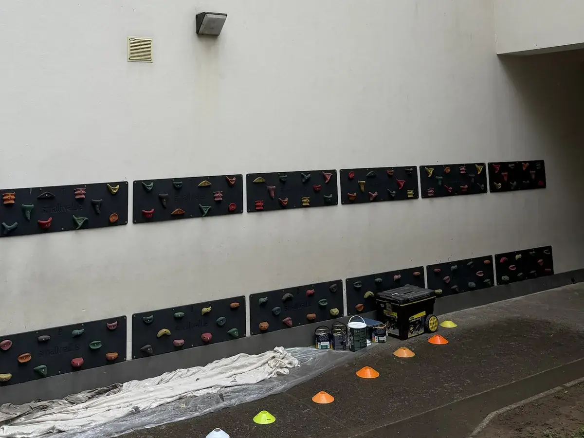 A blank rendered wall with two rows of climbing holds fixed to it, before painting