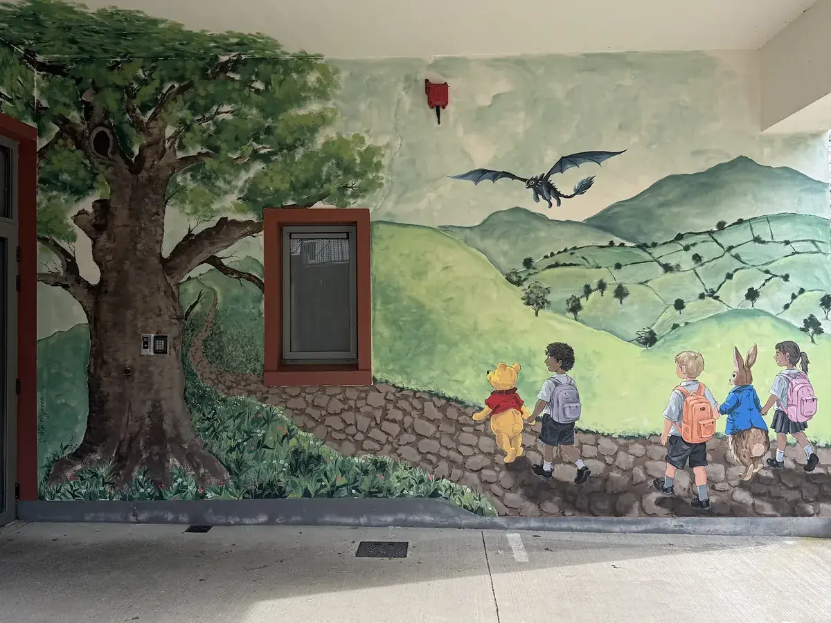 The same wall painted with a great oak, rolling green hills and children walking with storybook characters