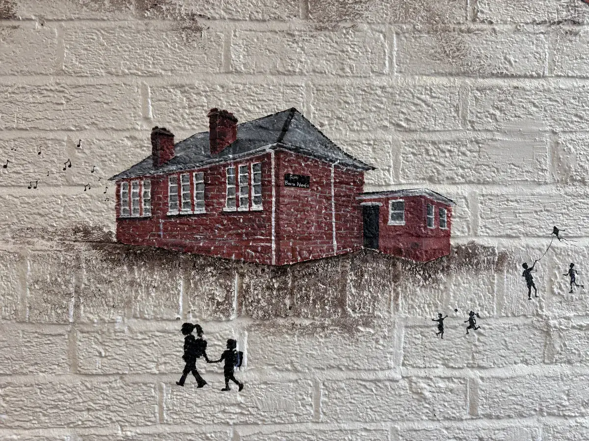 A painted red-brick schoolhouse with music notes drifting from it and children flying a kite