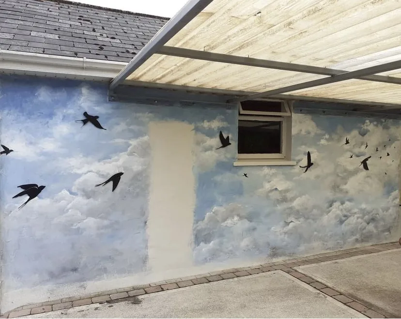 Swallows in flight across a painted cloudy sky on a sheltered garden wall